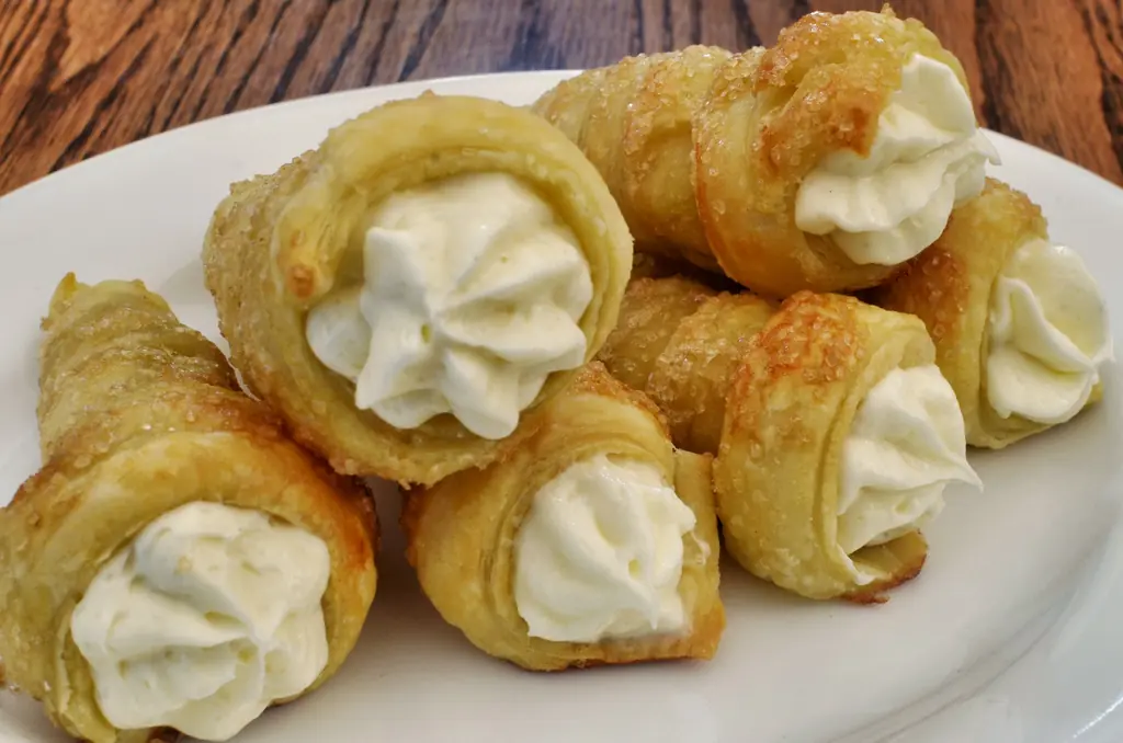 Puff pastry cream horns with piped white filling on a plate