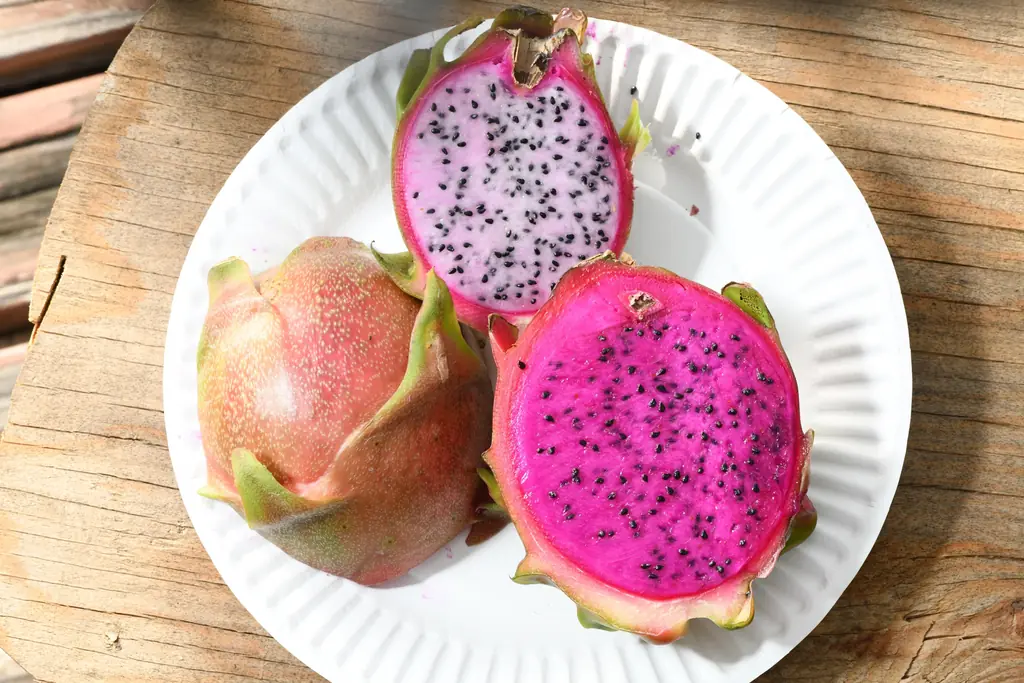 Red-fleshed and white-fleshed dragon fruit cut open on a plate, with pink-skinned whole fruit