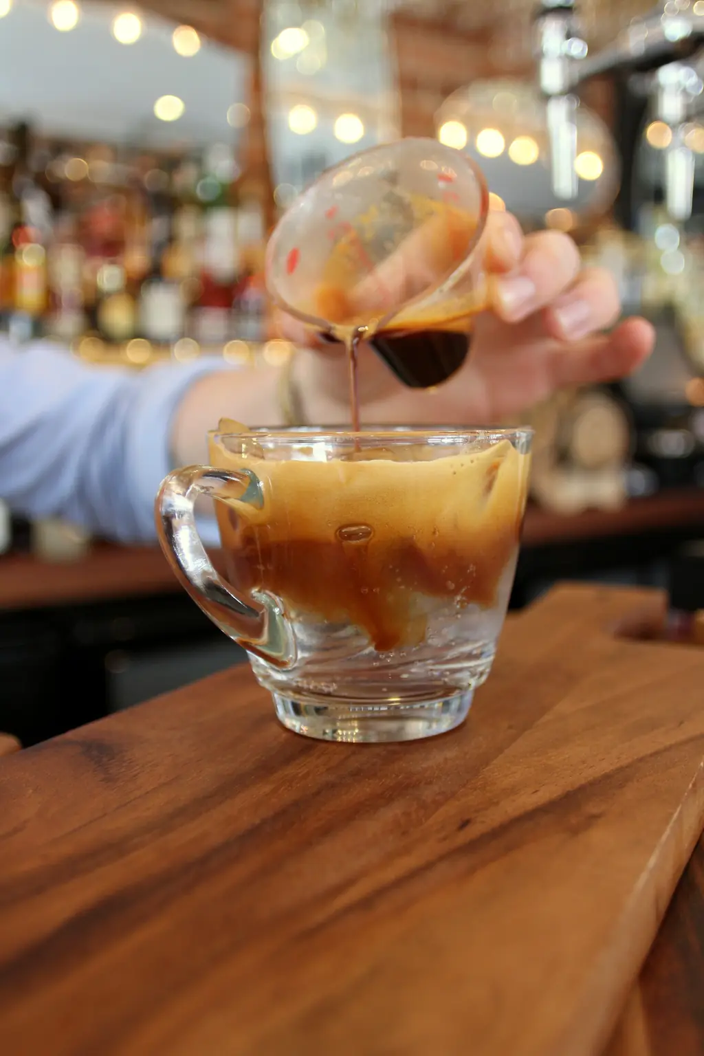 A bartender pouring espresso over tonic water and ice in a glass