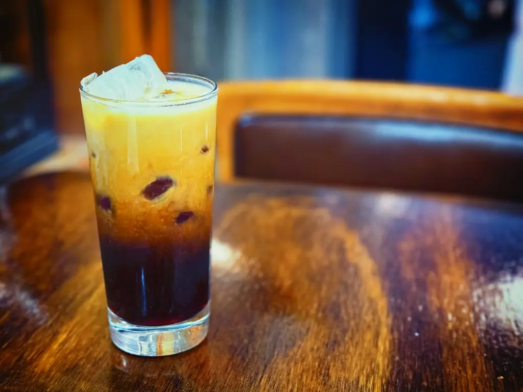 A tall glass of layered iced coffee on a wooden café table