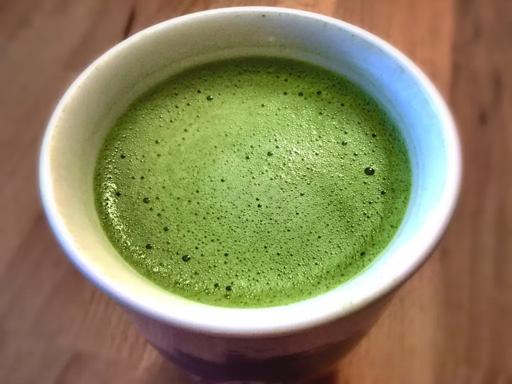 A cup of hot matcha latte with bright green foam on a wooden table