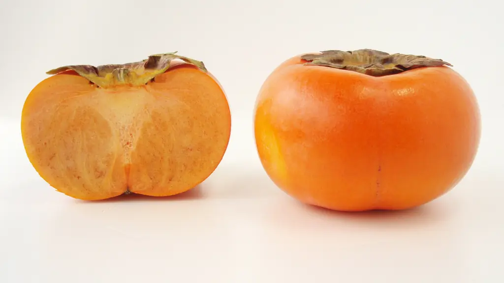 Ripe orange persimmons (Diospyros kaki), one whole and one cut in half