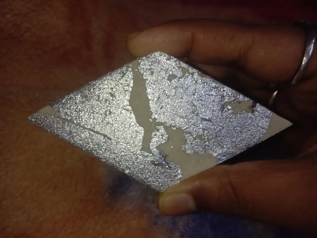 A diamond of kaju katli covered with a sheet of edible silver leaf (chandi ka varq), held in the hand