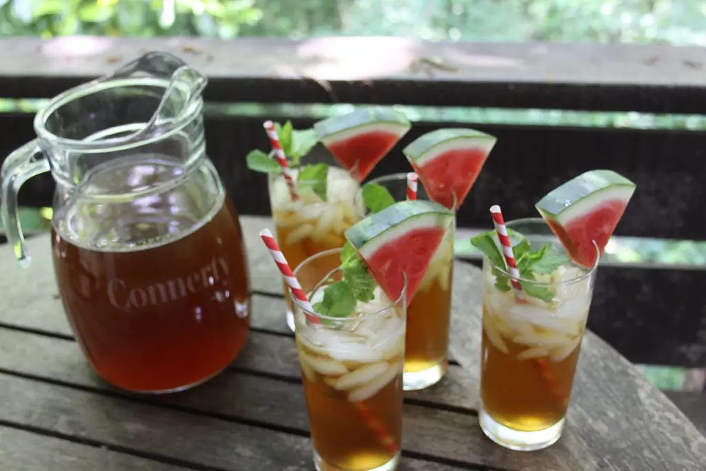 Glasses of iced drinks garnished with watermelon wedges and fresh mint sprigs on an outdoor table